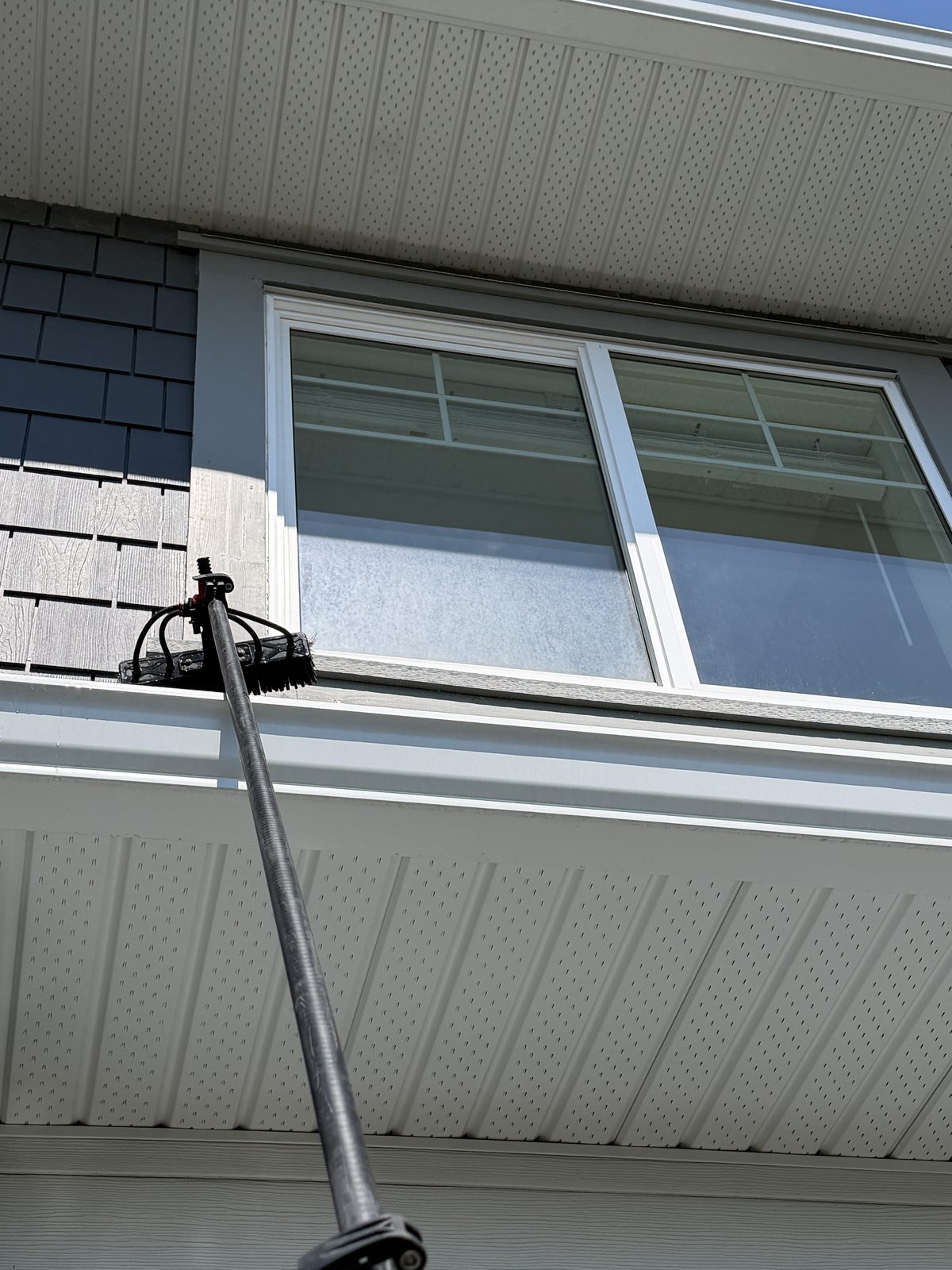 Water-fed pole brush cleaning a second-storey window from the ground